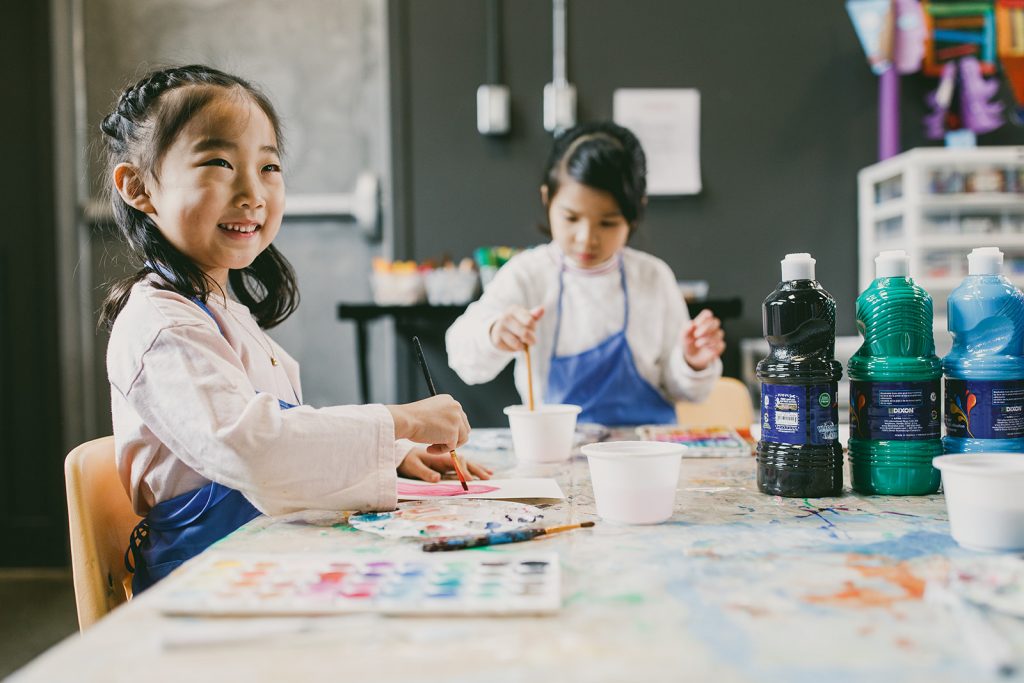 young girl smiling while painting at an art class