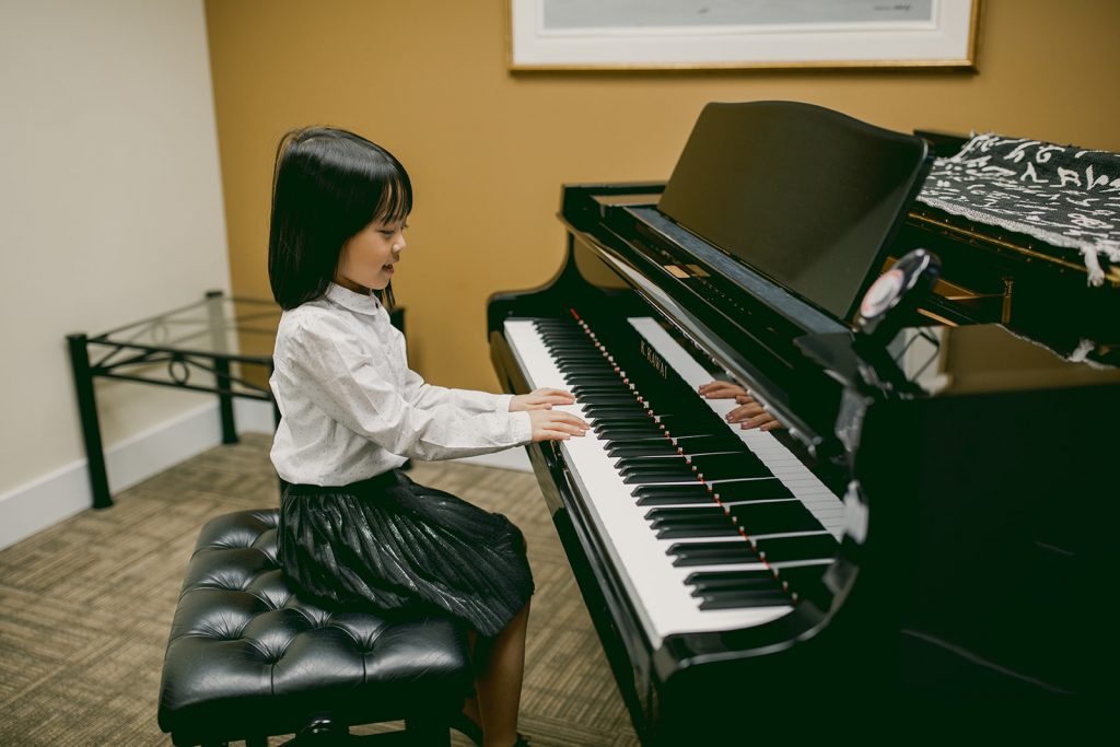 a seven year old girl playing piano at a studio